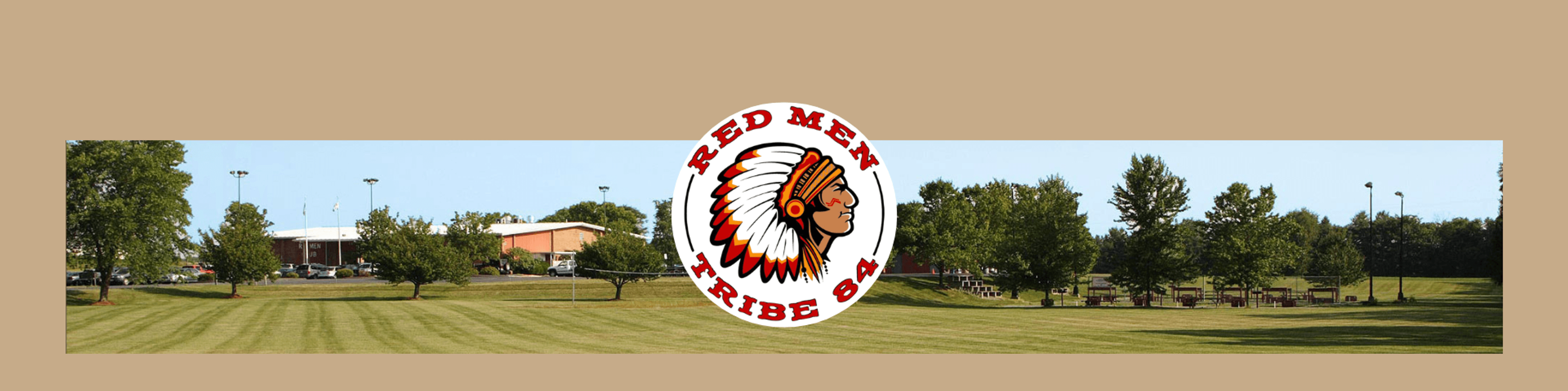 A wide panoramic view of a sports field with manicured grass, trees, and school buildings in the background. The Red Men Tribe 84 logo featuring a Native American chief's head in a circle is overlaid in the center.