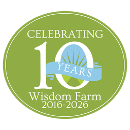 Green circular badge commemorating 10 years of Wisdom Farm from 2016-2026, featuring white text and a blue ribbon with sun design.