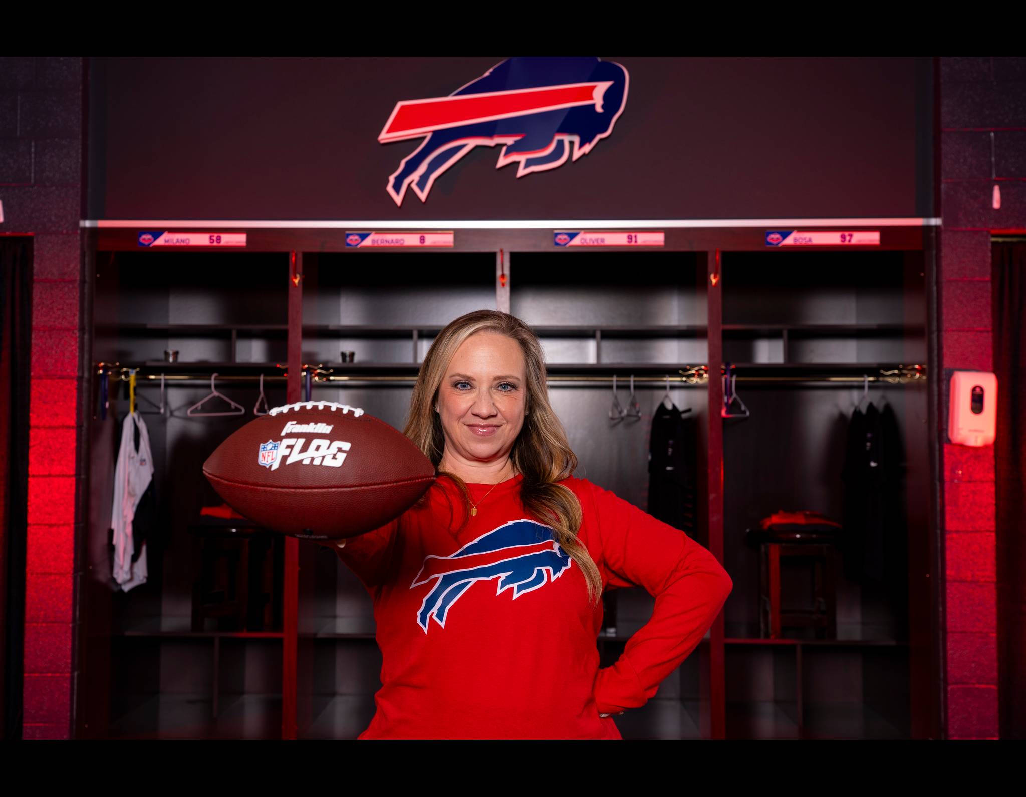 Woman in red Buffalo Bills sweater holding NFL FLAG football in team locker room with Bills logo