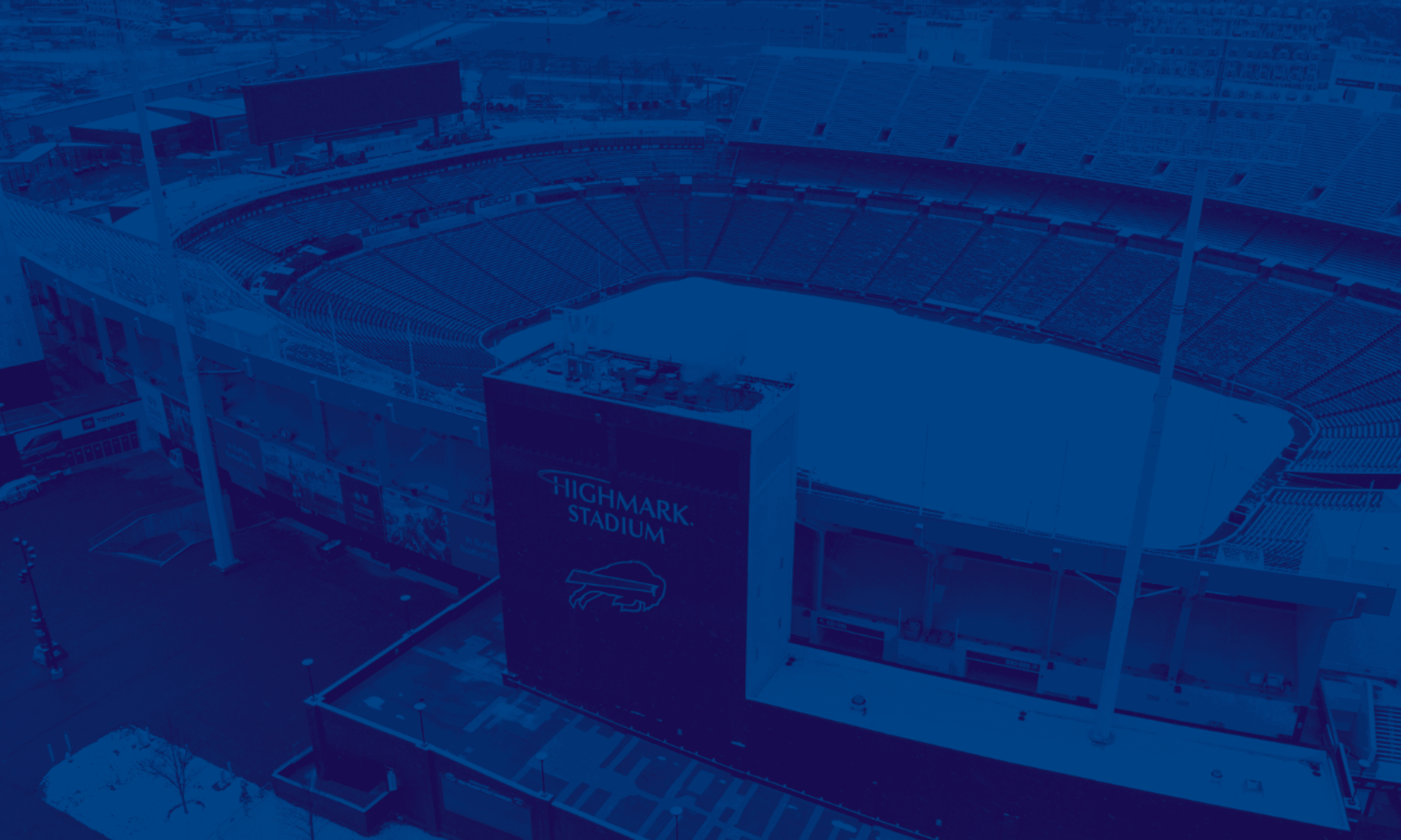 Aerial view of Highmark Stadium, a large sports venue with blue seating, ice rink, and surrounding structures, bathed in blue tones.