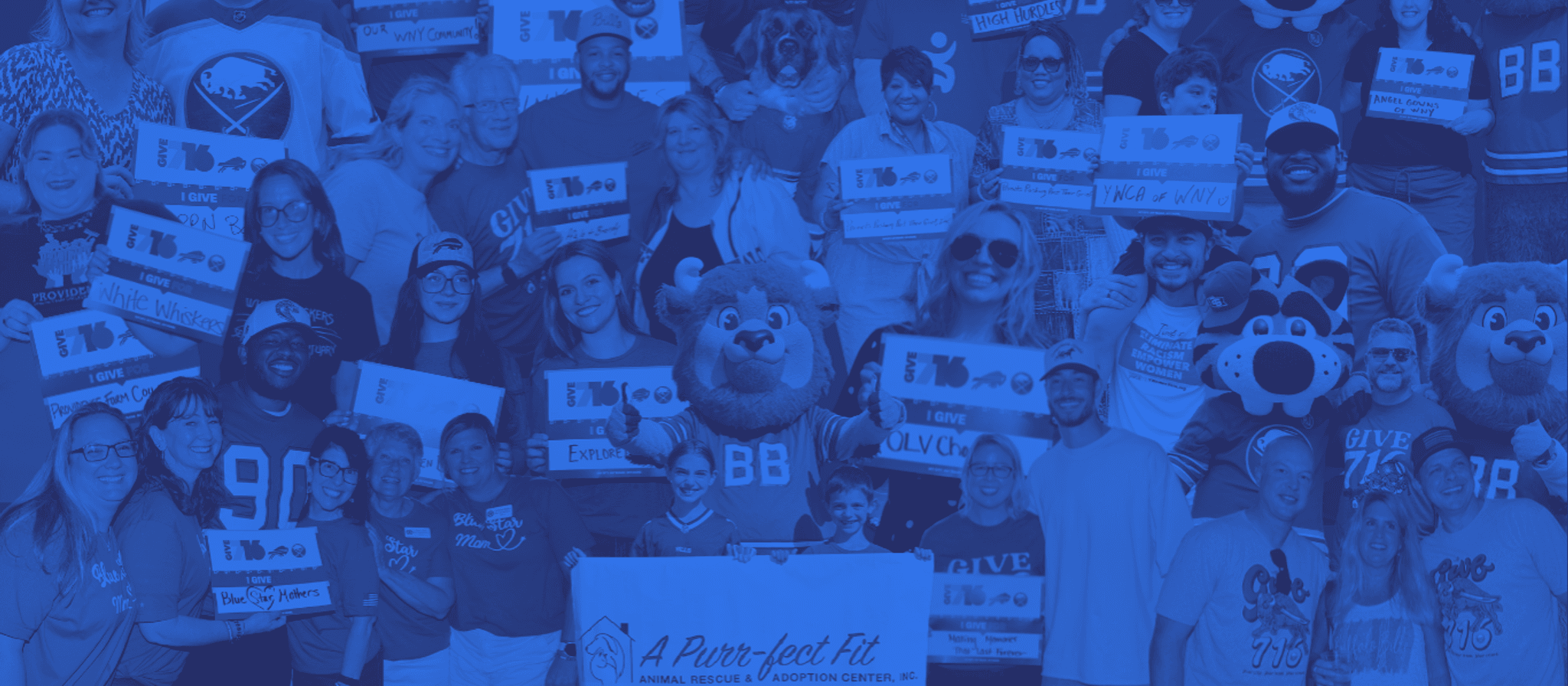Large group of people and mascots in blue uniforms holding signs at a charity event for an animal rescue and adoption center.