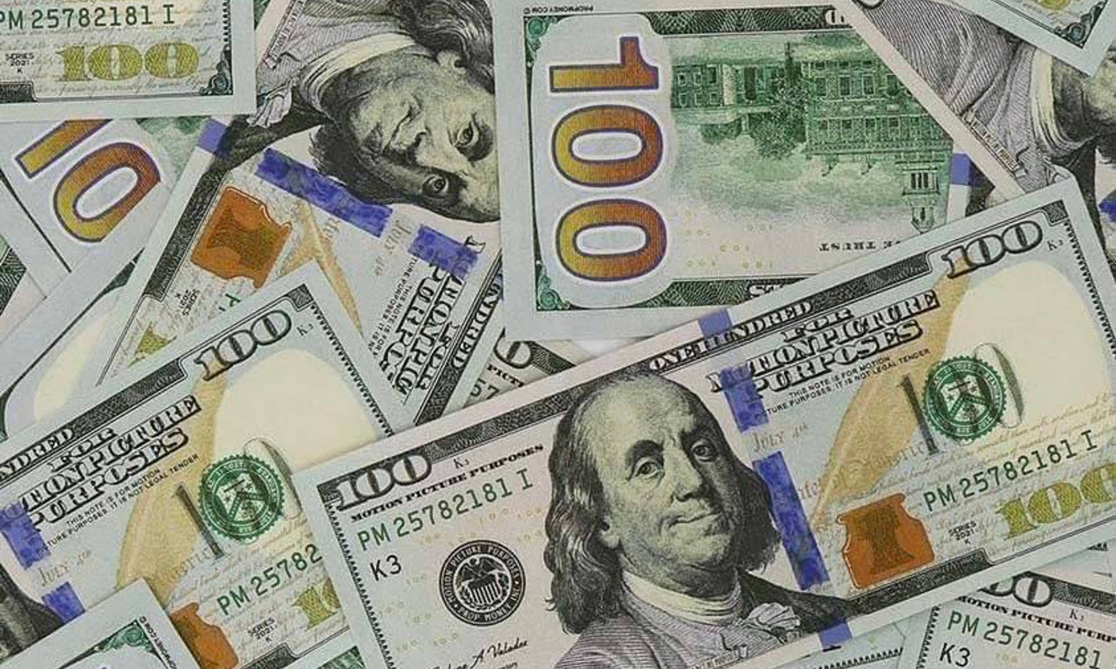 Multiple one hundred dollar bills overlapping each other, displaying portraits of Benjamin Franklin and architectural details from the currency.