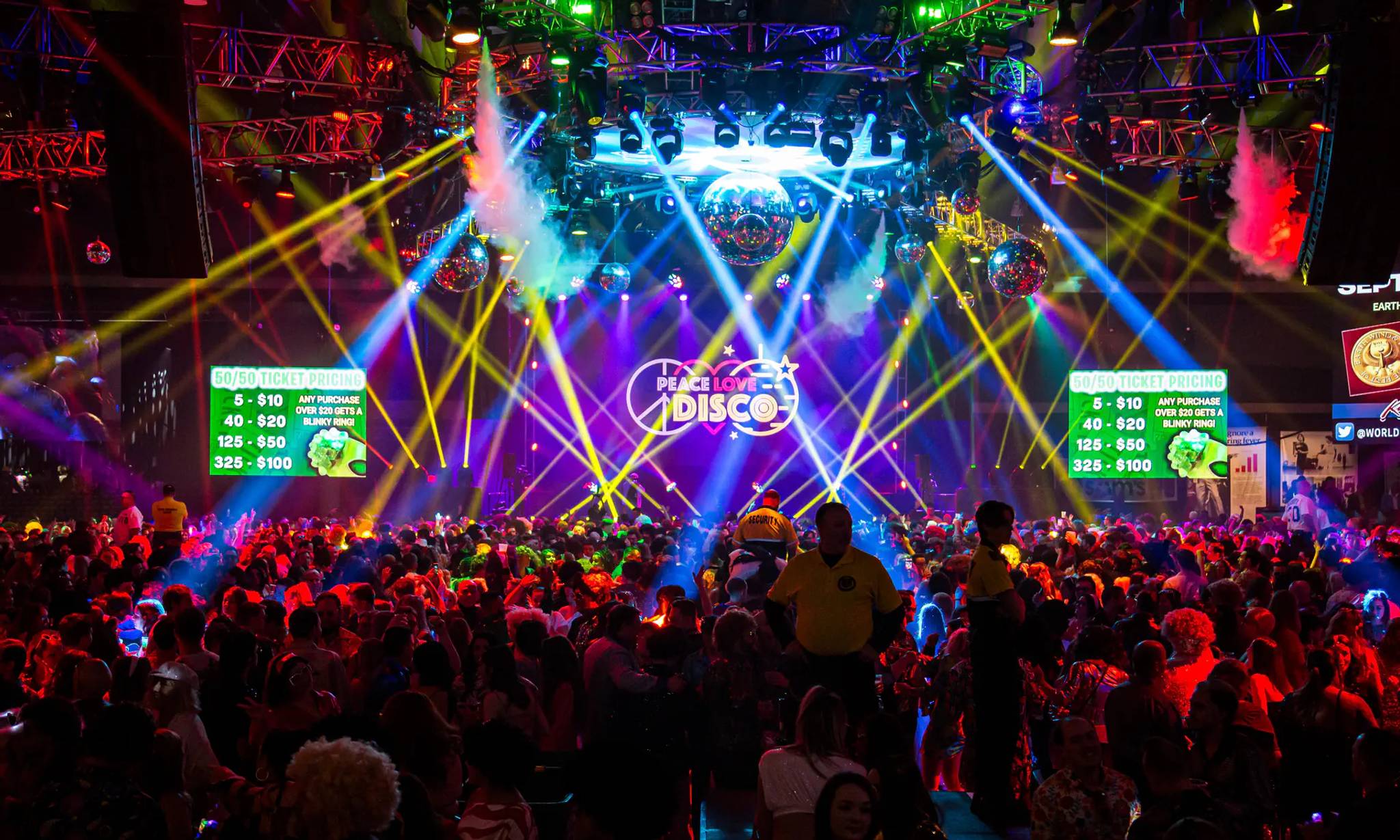 A vibrant disco dance event with massive crowds enjoying colorful laser light shows, disco balls, and dynamic stage lighting in multiple colors including red, blue, yellow, and green.