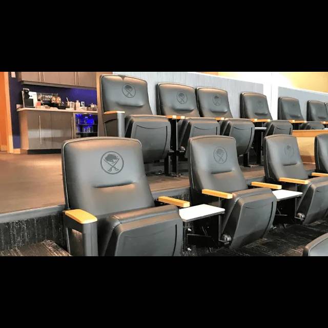 Modern theater seating with gray upholstered chairs featuring yellow accents and attached white tables, arranged in rows facing a screen in a contemporary cinema auditorium.