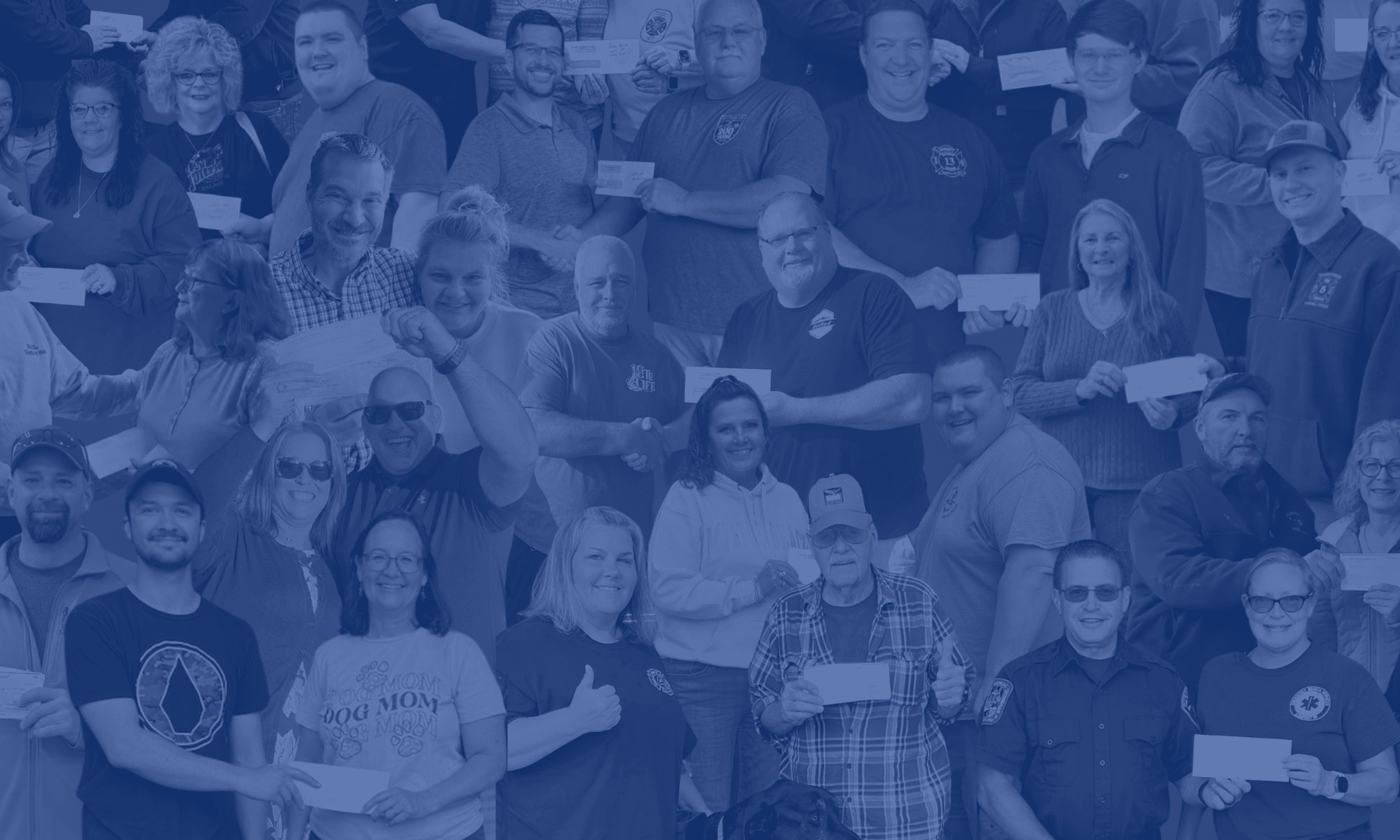 Large diverse group of people smiling at camera, many holding envelopes or certificates, gathered together in blue-toned group photo.