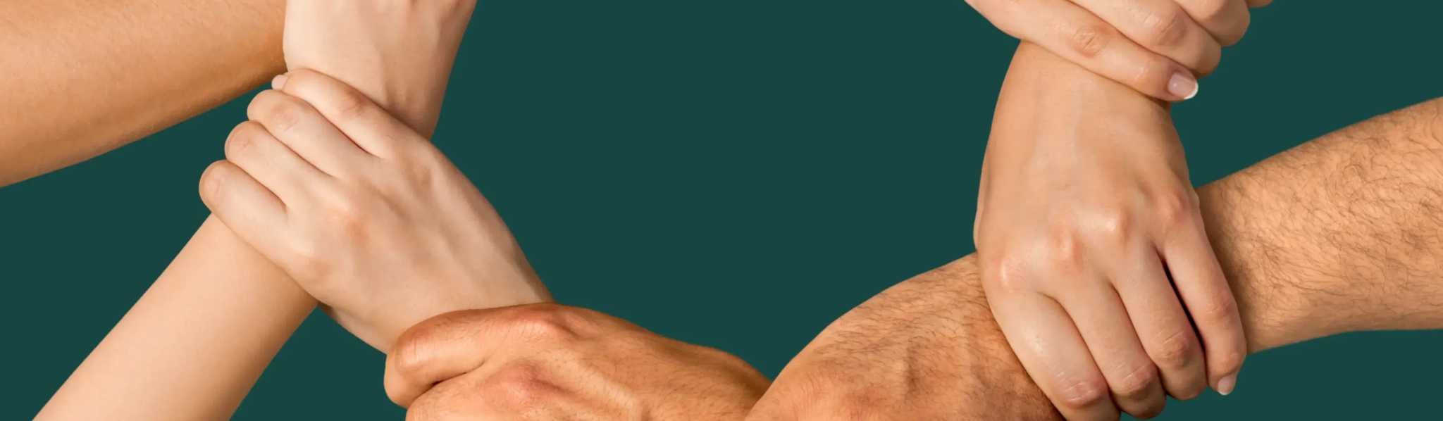 Multiple hands joined together in a circle against a teal background, symbolizing unity, teamwork, and collaboration among diverse people.