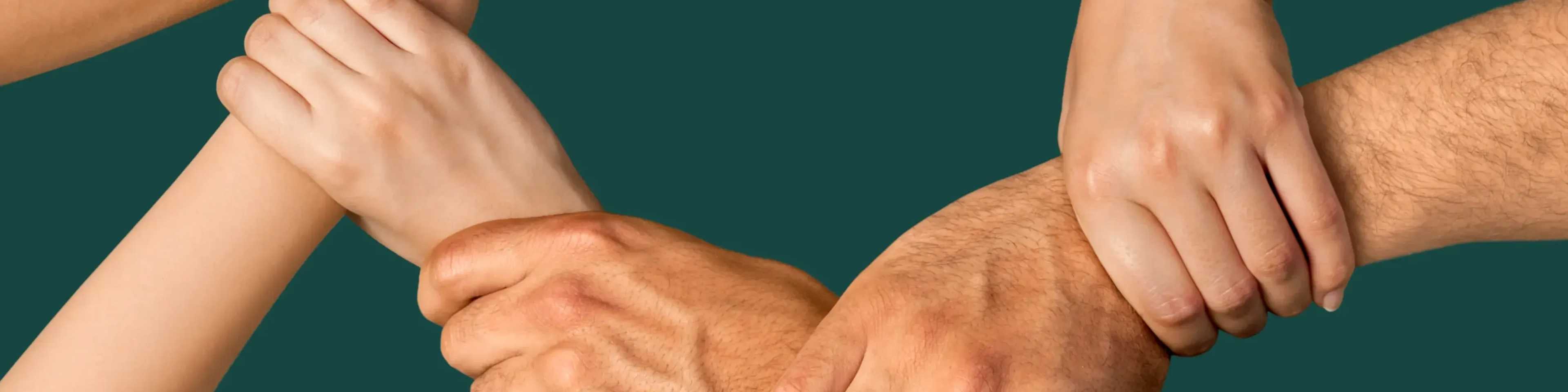 Multiple hands joined together in a circle against a teal background, symbolizing unity, teamwork, and collaboration among diverse people.