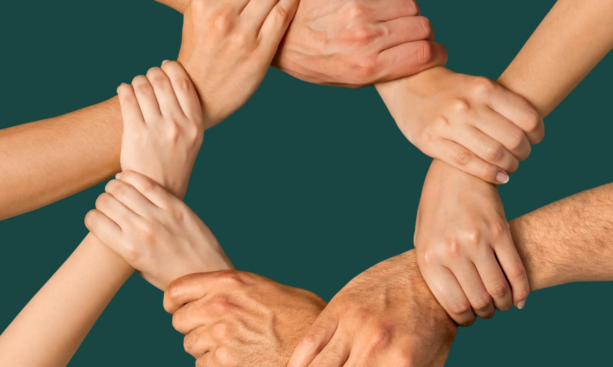 Multiple hands joined together in a circle against a teal background, symbolizing unity, teamwork, and collaboration among diverse people.