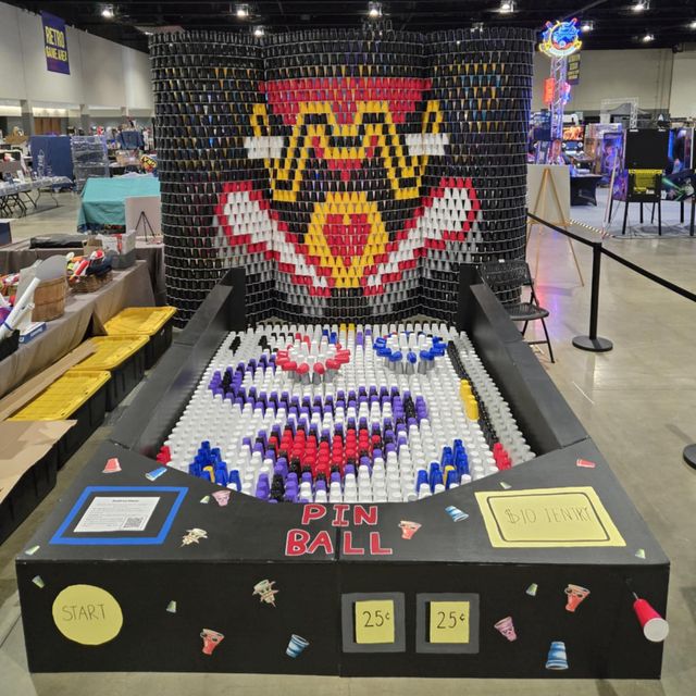 Large pinball machine made entirely of colorful cups in a convention center, featuring intricate cup mosaic design.