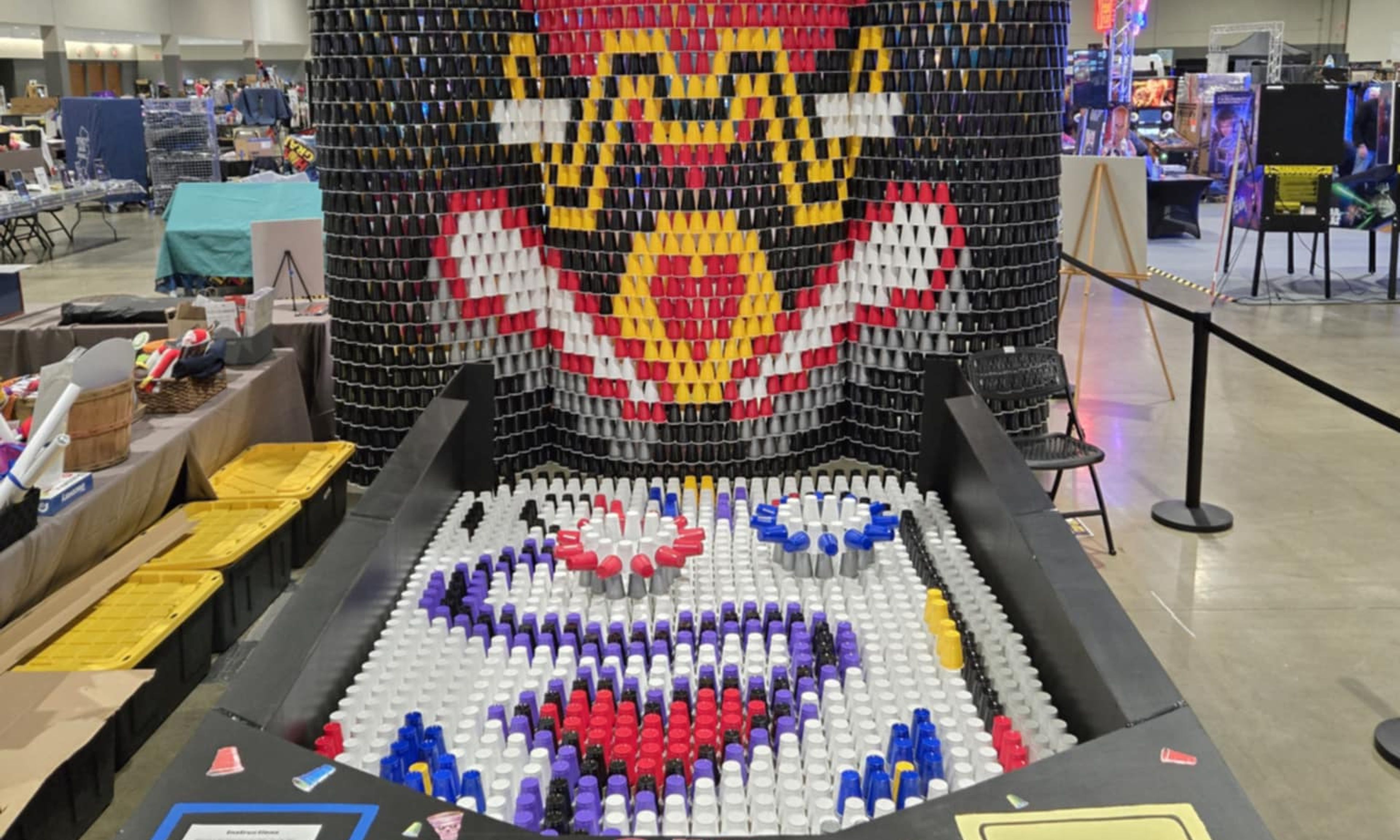 Large pinball machine made entirely of colorful stacked cups in convention center with elaborate design and scoring area