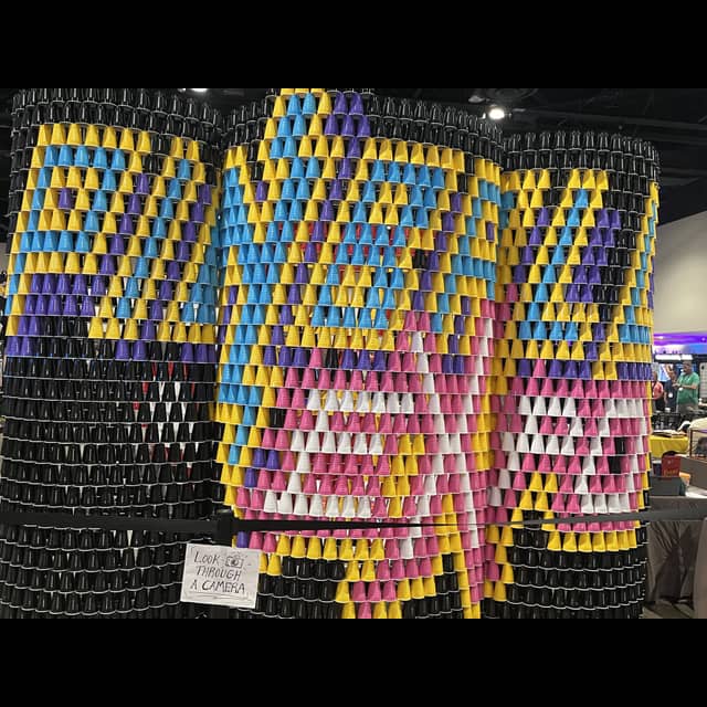 Large colorful mosaic art installation made of stacked paper/plastic cups in blue, yellow, purple, pink, and white.